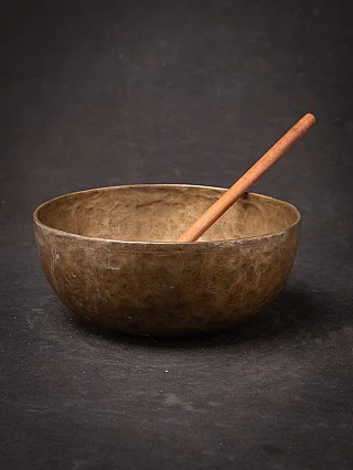 Nepali bronze singing bowl with wooden mallet resting inside, three-quarter view