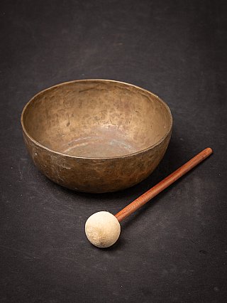 Nepali bronze singing bowl with felt mallet in the foreground, three-quarter view