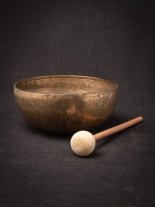 Nepali bronze singing bowl with mallet placed in front, angled view