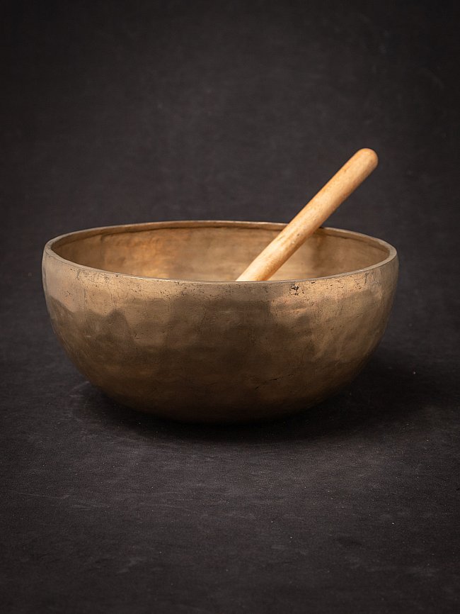 Large antique bronze Nepali singing bowl with wooden mallet resting inside, angled view