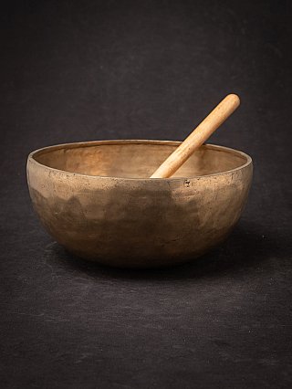 Large antique bronze Nepali singing bowl with wooden mallet resting inside, angled view