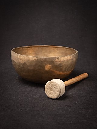 Nepali bronze singing bowl with felt mallet placed in front on the surface, low angle