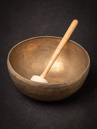 Bronze Nepali singing bowl with wooden mallet leaning inside, three-quarter view