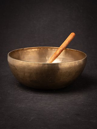Nepali bronze singing bowl with wooden mallet resting inside, angled view