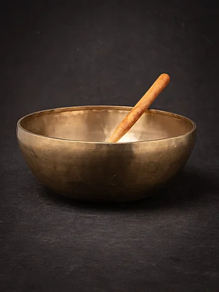 Nepali bronze singing bowl with wooden mallet resting inside, angled view