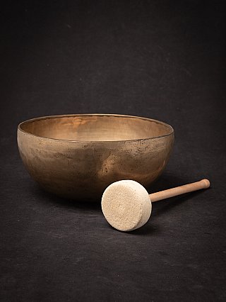 Nepali bronze singing bowl with mallet in front, bowl behind on dark background