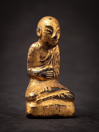 Antique wooden Burmese monk statue with worn gilding, three-quarter view of folded hands