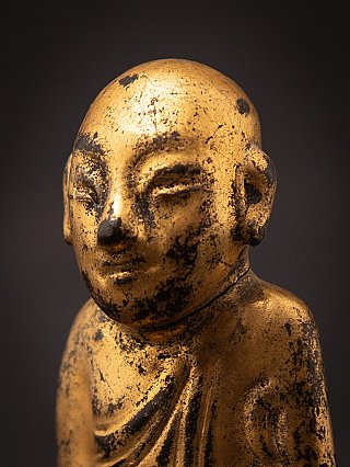 Face detail of the wooden Burmese monk statue in three-quarter view with visible ear