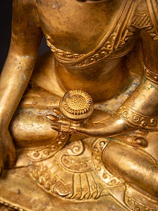 Detail of the left hand holding the bowl and the engraved robe border on the bronze Buddha
