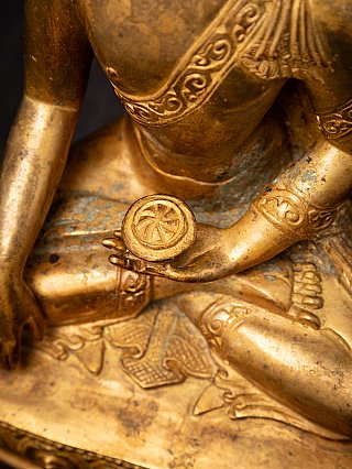 Detail of the left hand holding a bowl on the lap, with engraved patterns on the bronze