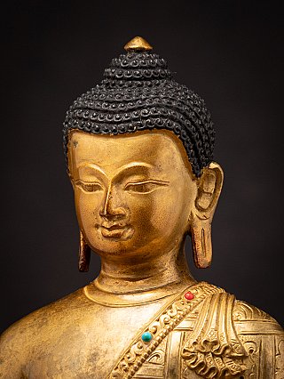 Three-quarter face detail of the Buddha statue with elongated earlobe and inlaid robe trim