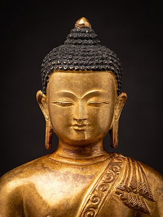 Frontal face detail of the Nepali bronze Buddha, showing hair curls and elongated ears