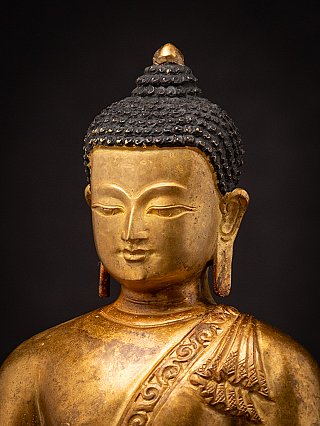Three-quarter face detail of the Nepali bronze Buddha, with robe band visible on the shoulder