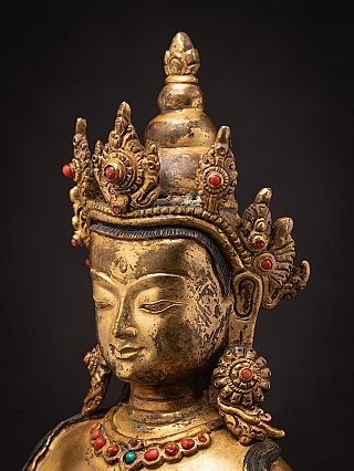 Three-quarter face close-up of the Nepali bronze Buddha showing crown ornaments