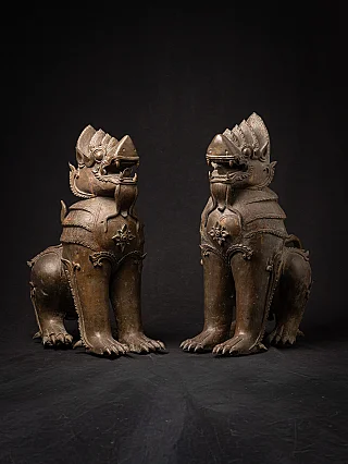 Pair of Burmese bronze temple lion statues, seated, facing each other in three-quarter view