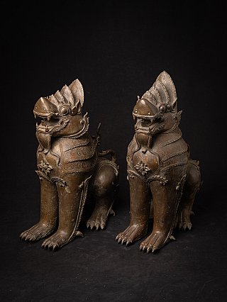 Pair of Burmese bronze temple lion statues, seated, angled view highlighting the legs and paws