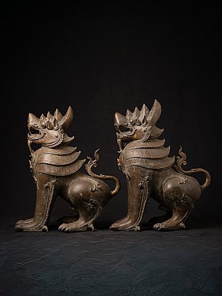 Burmese bronze temple lion statues, side view showing curled tails and layered armor