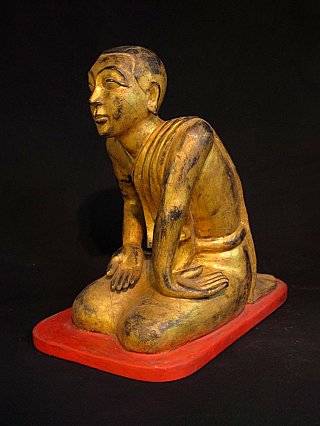 Single wooden monk statue from Burma (Myanmar), seated on a red base, three-quarter view