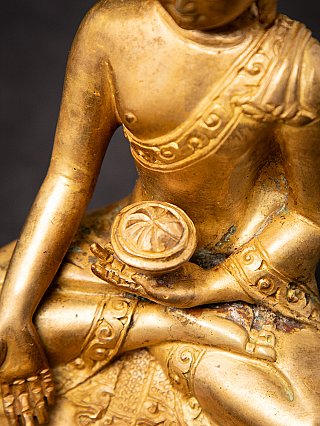Hand holding a bowl detail on the Nepali bronze Buddha statue, showing wear and patina