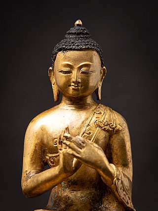 Close-up of head and torso of the Nepali bronze Buddha, hands raised at chest
