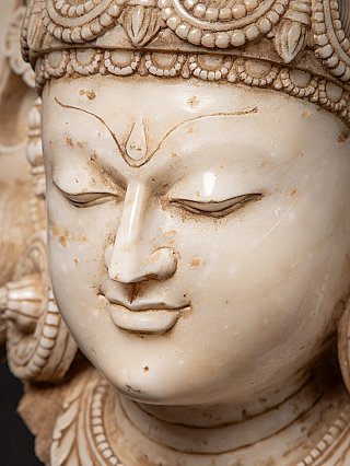 Marble face detail showing the nose, lips, and downcast eyes of the Bodhisattva head