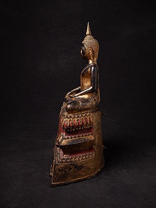 Thai bronze Buddha statue seated, side profile view with the tall base in silhouette