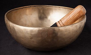 Nepali bronze singing bowl with wooden striker resting inside, angled view