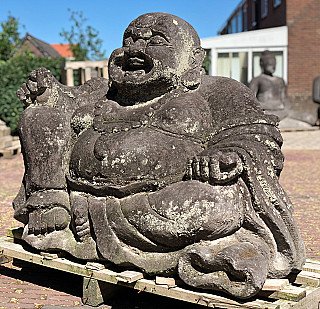 Happy Buddha statue in lavastone, seated three-quarter view with raised left hand
