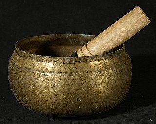 Nepali bronze singing bowl with wooden striker resting inside, angled side view
