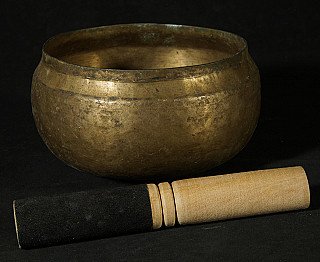 Nepali bronze singing bowl with striker placed in front on black cloth, three-quarter view