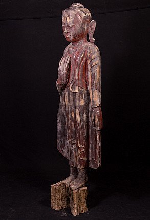 Wooden Buddha statue from Myanmar in three-quarter view, showing worn painted surface
