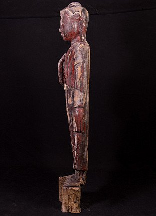 Burmese wooden Buddha statue in left side profile, standing on a rough wooden base