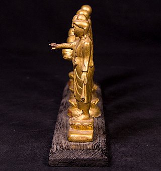 Staande houten Boeddha uit Myanmar in zijaanzicht, arm naar voren, monniken op rij