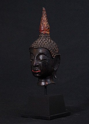 Bronze Buddha head from Thailand in three-quarter view, showing elongated earlobe and red-painted lips